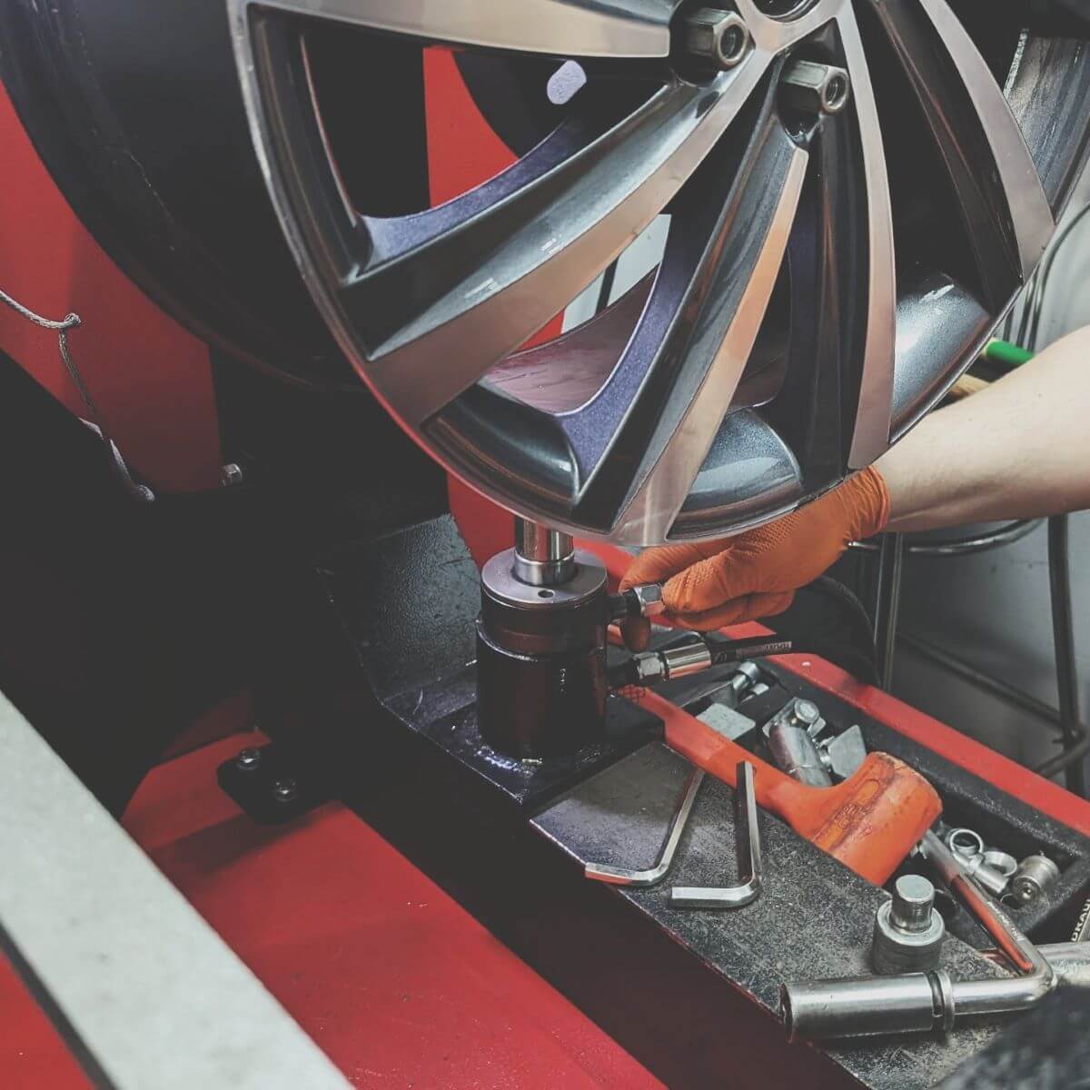 Specjalista prezentuje proces prostowania krawędzi felgi aluminiowej przy użyciu siłownika hydraulicznego podczas szkolenia technicznego